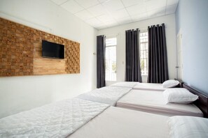 A hotel room with two beds, a flat-screen TV mounted on a wooden wall, and a window with curtains.