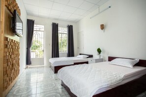 Ein Hotelzimmer mit zwei Betten, einem an einer Ziegelwand befestigten Fernseher, einer Topfpflanze und einem Fenster mit Vorhängen.