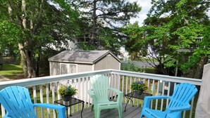 A wooden deck with blue chairs and a table, surrounded by white railings and trees. - Charming 4BR TH – Steps to Downtown & Boardwalk Fun–Bethany Winds, Bethany Beach (Bethany Beach)