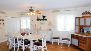 A dining area with a wooden table and white chairs, a ceiling fan, and a cabinet with glass doors. - Charming 4BR TH – Steps to Downtown & Boardwalk Fun–Bethany Winds, Bethany Beach (Bethany Beach)