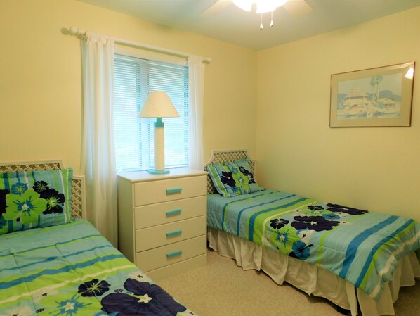 Un dormitorio con dos camas individuales, una mesita de noche, una lámpara y una ventana con persianas.