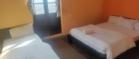 A room with two beds, a window with curtains, and a door.