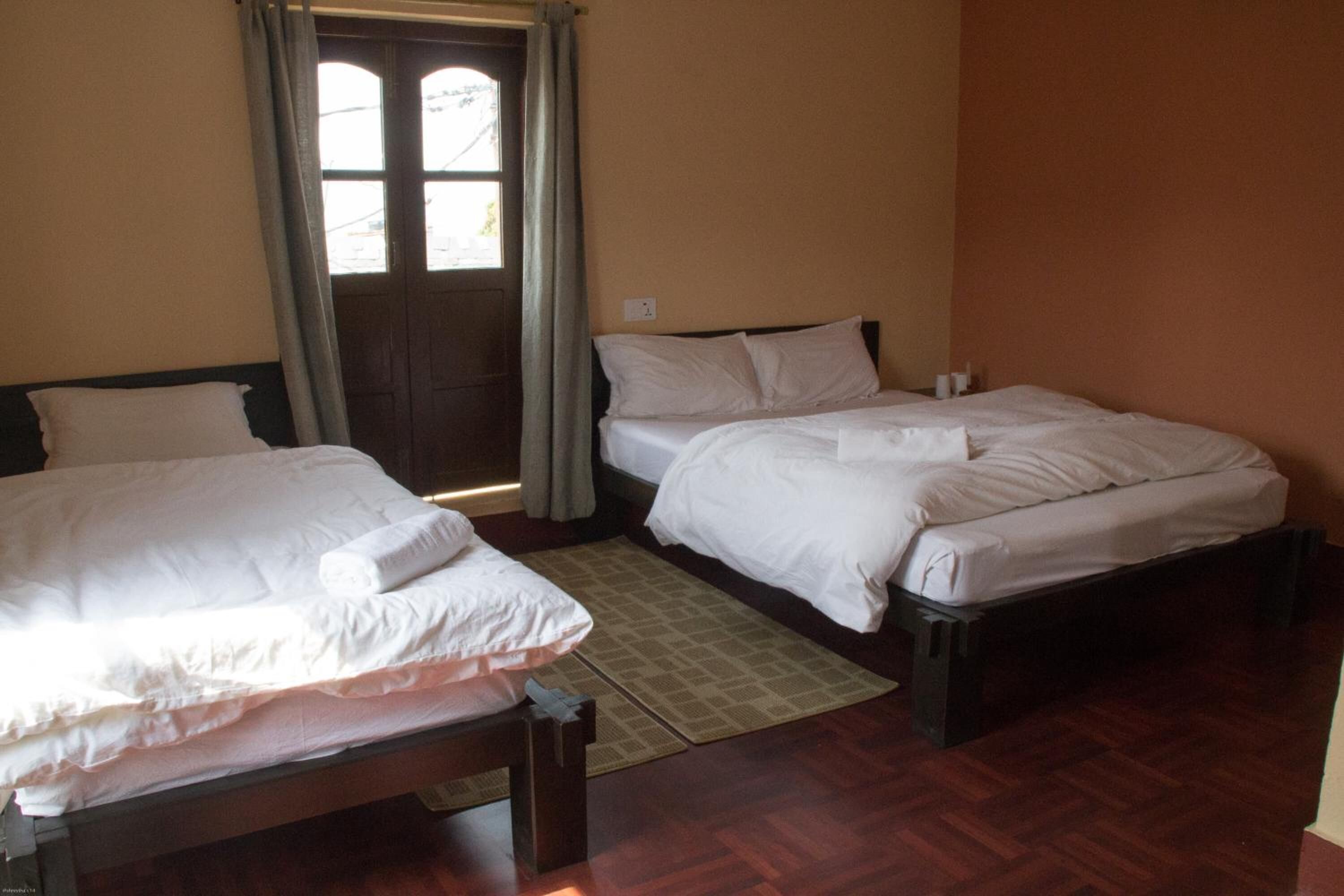 A room with two beds, a wooden floor, a window with curtains, and a door.