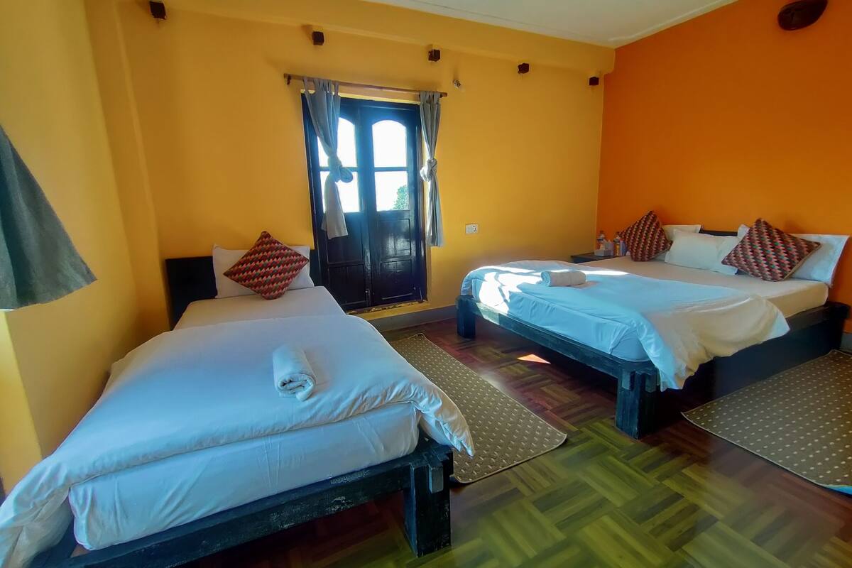 A hotel room with two beds, a window with curtains, wooden flooring, and a small rug.