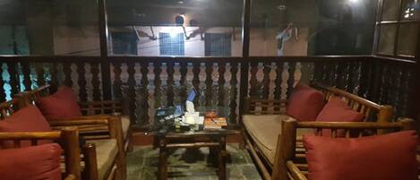 Un balcón con muebles de madera, una mesa de vidrio y vista a un edificio iluminado.