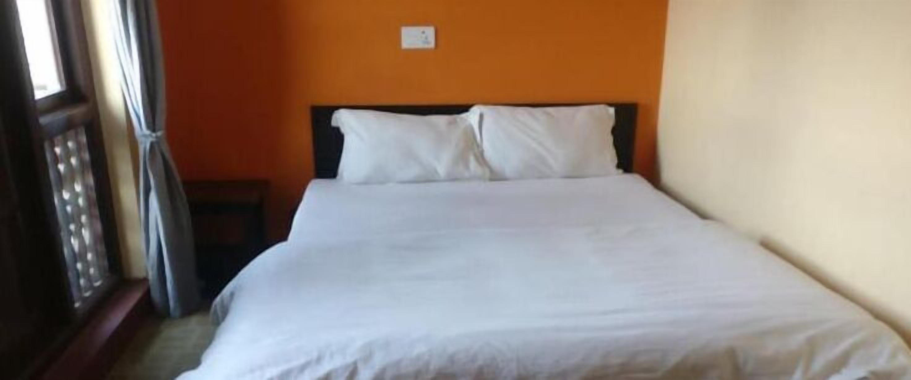 A single bed with white bedding in a room with orange walls.