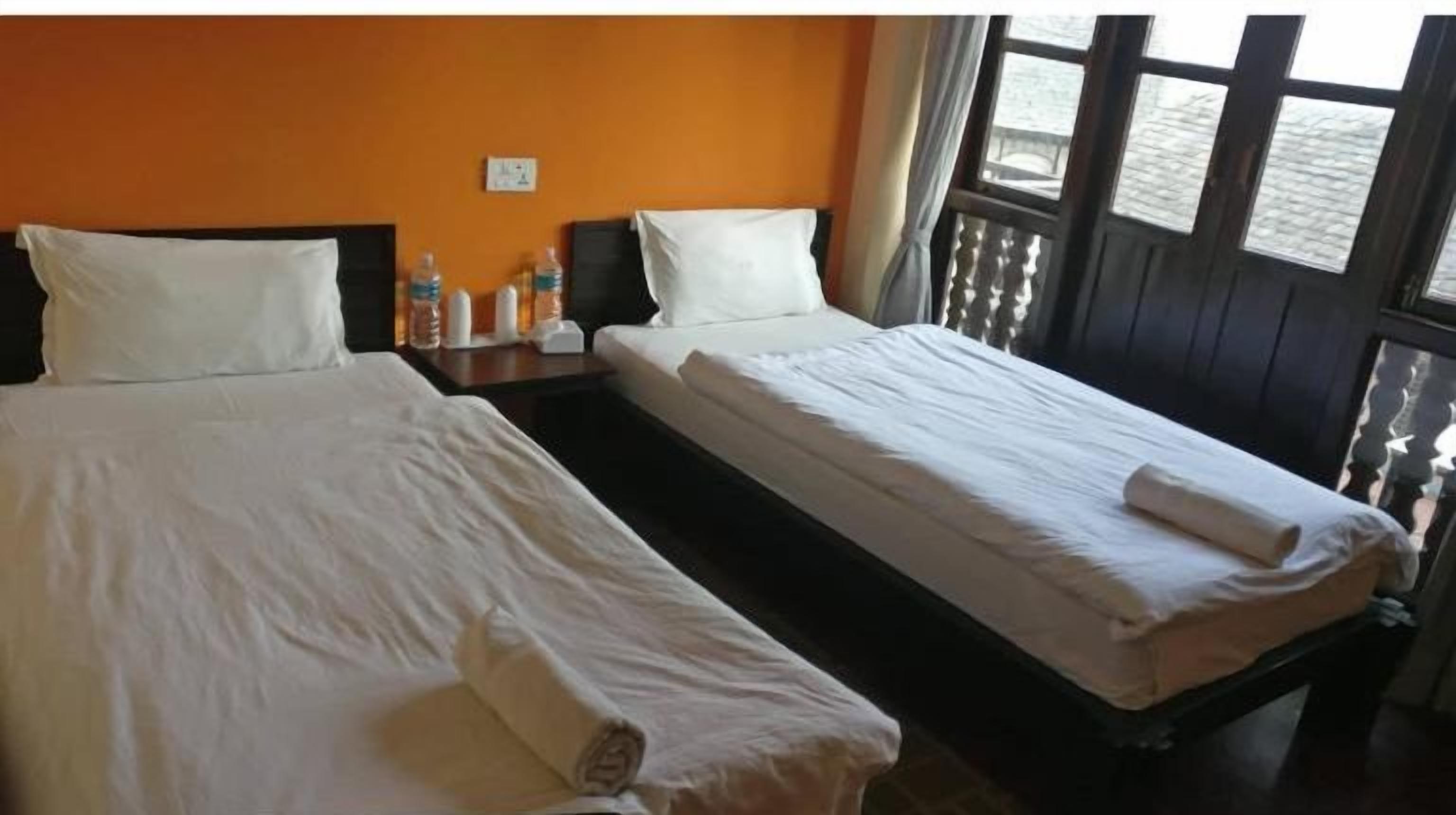 A twin bed room with two beds, a nightstand, and a window with curtains.