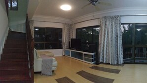 A spacious living room with a staircase, a sofa, a TV, and large windows. - KK City HomeSuite at KK City Center 1 (Kota Kinabalu)