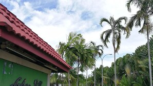 A building with a green facade and a red roof, surrounded by lush greenery and palm trees. - KK City HomeSuite at KK City Center 1 (Kota Kinabalu)