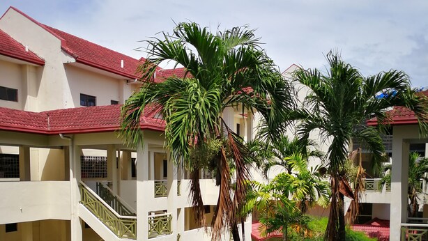 A multi-level building with a red-tiled roof, surrounded by lush greenery and palm trees. - KK City HomeSuite at KK City Center 1 (Kota Kinabalu)