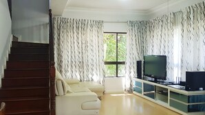 A living room with a staircase, a sofa, a TV, and curtains. - KK City HomeSuite at KK City Center 1 (Kota Kinabalu)