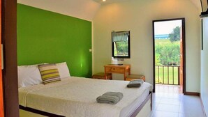 A bedroom with a bed, a small table, a TV, and a balcony with a view of greenery. - Kiangtan Houses (Pluak Daeng)