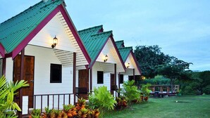 A row of white cabins with green roofs and purple trim, surrounded by lush tropical plants. - Kiangtan Houses (Pluak Daeng)