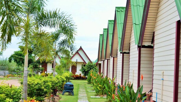 A row of bungalow-style hotel rooms with a pathway leading to the entrance, surrounded by lush greenery and palm trees. - Kiangtan Houses (Pluak Daeng)