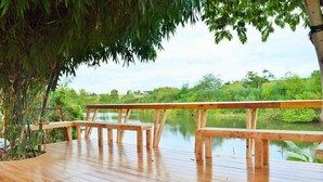 A wooden deck with benches overlooking a calm body of water, surrounded by lush greenery. - Kiangtan Houses (Pluak Daeng)