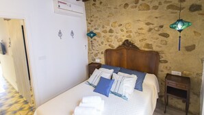 A bedroom with a stone wall, a wooden headboard, a bed with white bedding and blue pillows, two bedside tables, and two hanging lamps. - SUITE APARTMENT - 1 HABITACIÓN VISTAS A CALLE (Villajoyosa)