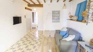 A living room with a grey sofa, patterned floor, wooden beams, a mounted TV, and a decorative wall piece. - SUITE APARTMENT - 1 HABITACIÓN VISTAS A CALLE (Villajoyosa)