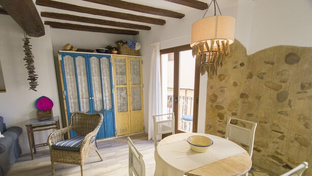 A room with a round wooden table, wicker chairs, a hanging lamp, a stone wall, and a blue-framed door. - SUITE APARTMENT - 1 HABITACIÓN VISTAS A CALLE (Villajoyosa)