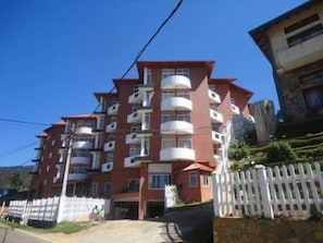 A multi-story building with balconies, a white picket fence, and a clear sky.