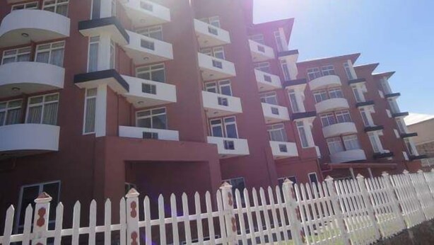 Un edificio residencial de varios pisos con balcones, una valla de piquetes blancos y un cielo despejado.