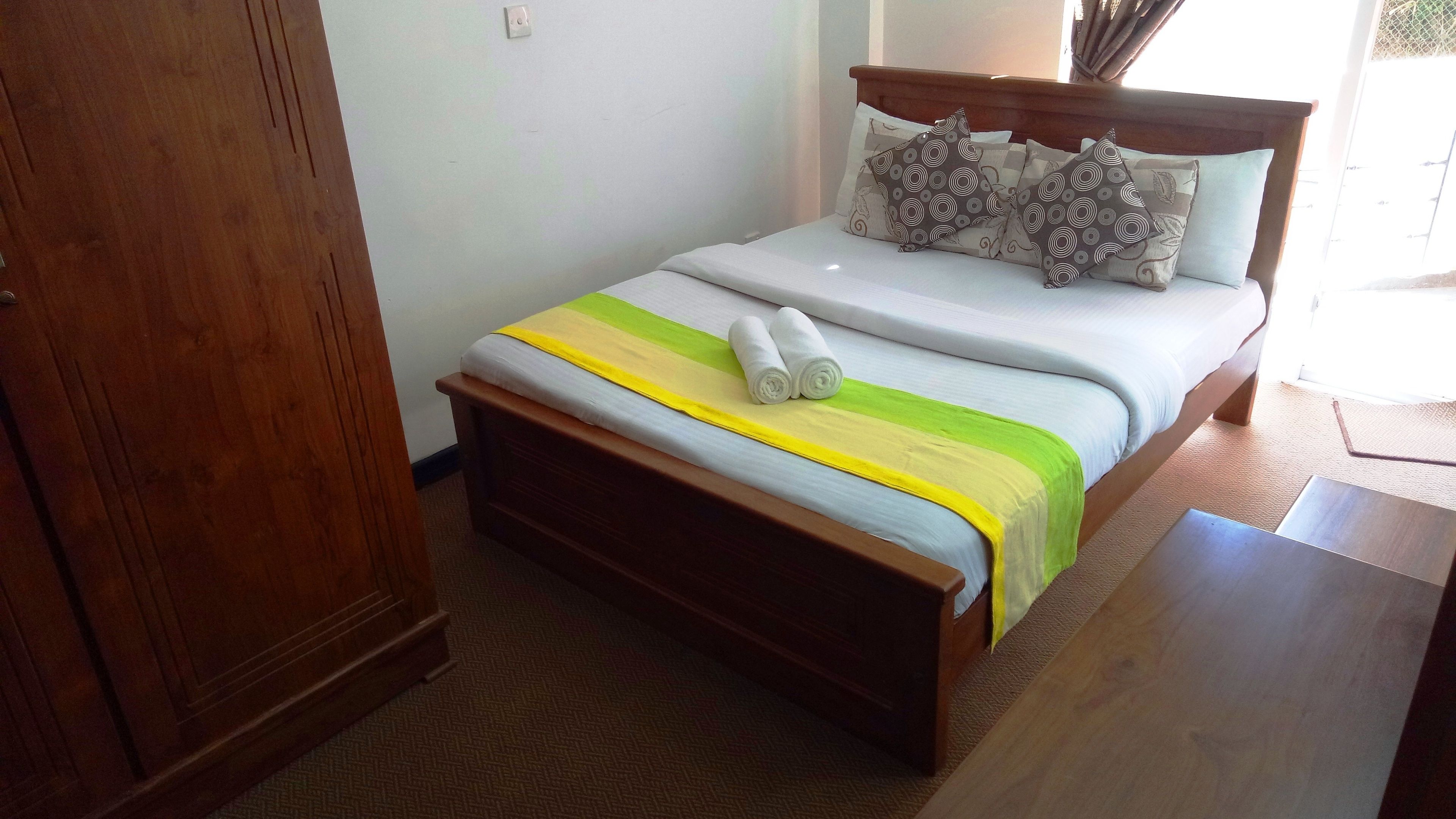 A neatly made bed with a striped bedspread, two rolled towels, and patterned pillows.