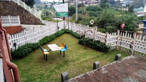Un jardín vallado con una mesa y sillas, un letrero que dice "ASHLEY HILLS NO:77", y una calle con vehículos.
