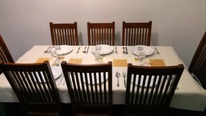 A dining table set for four with wooden chairs, white tablecloth, and basic tableware.