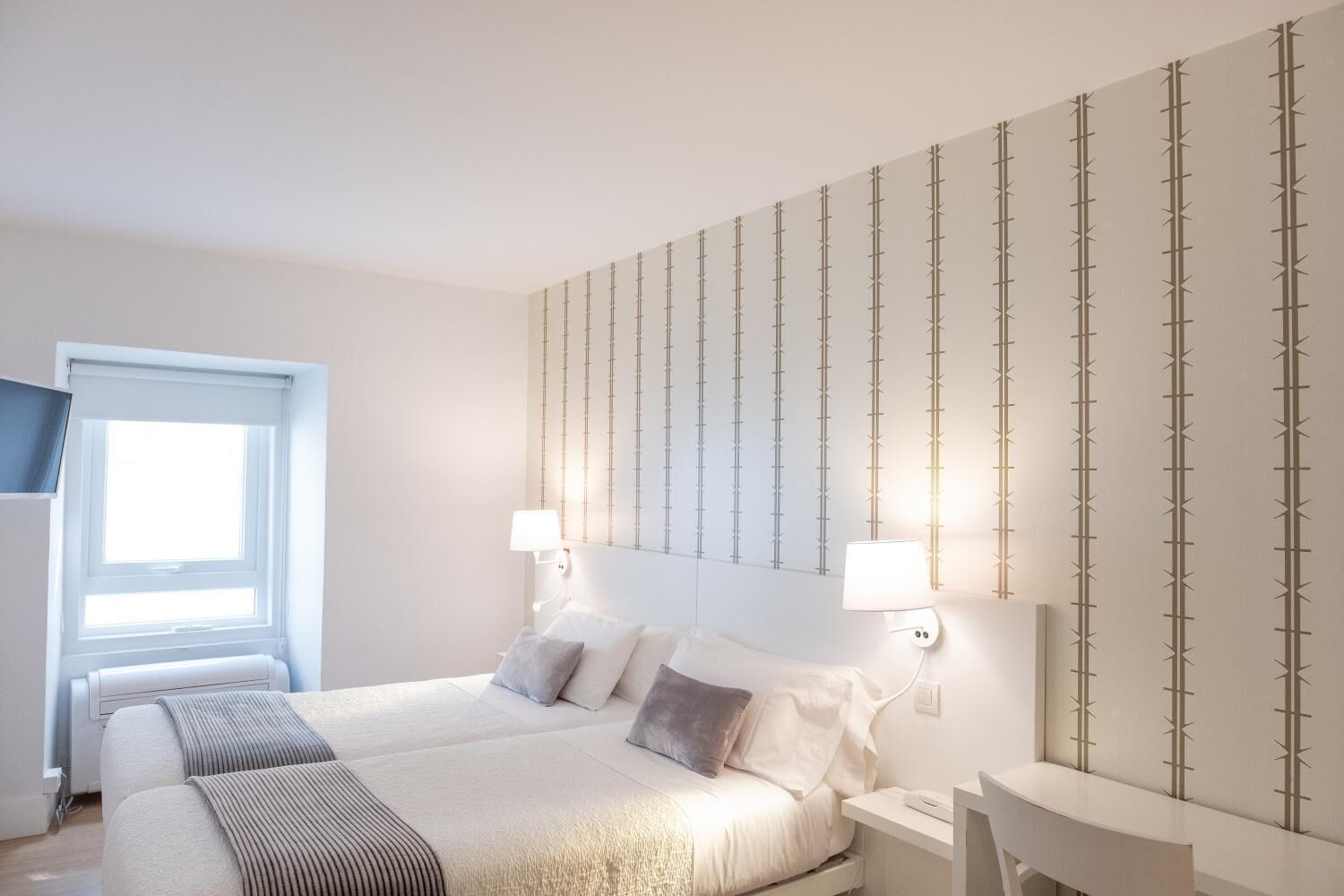 A hotel room with a large bed, two bedside tables, a desk, and a TV mounted on the wall.