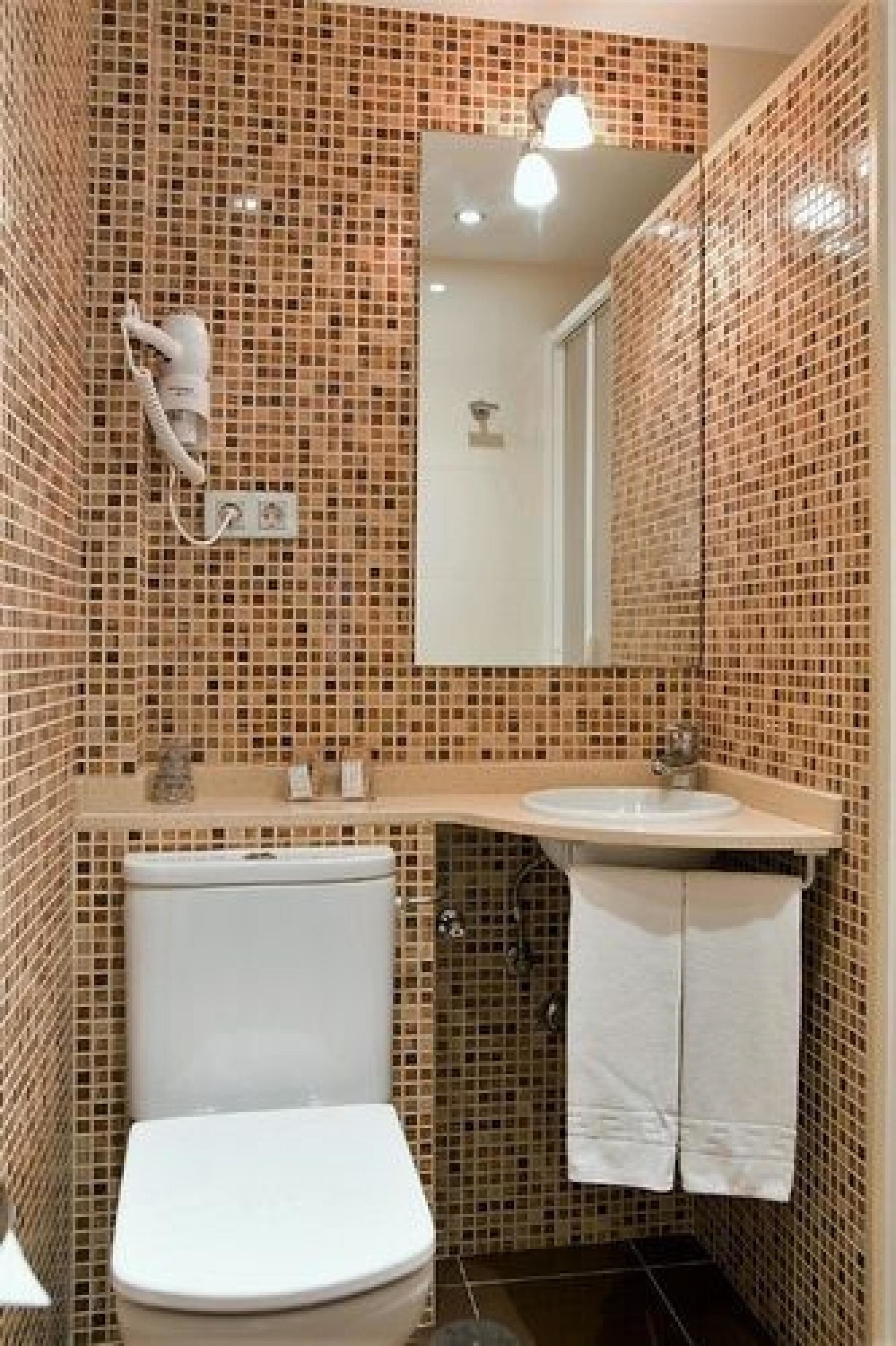 Un baño con pared de azulejos, un inodoro blanco, un lavamanos y una toalla colgada en la pared.