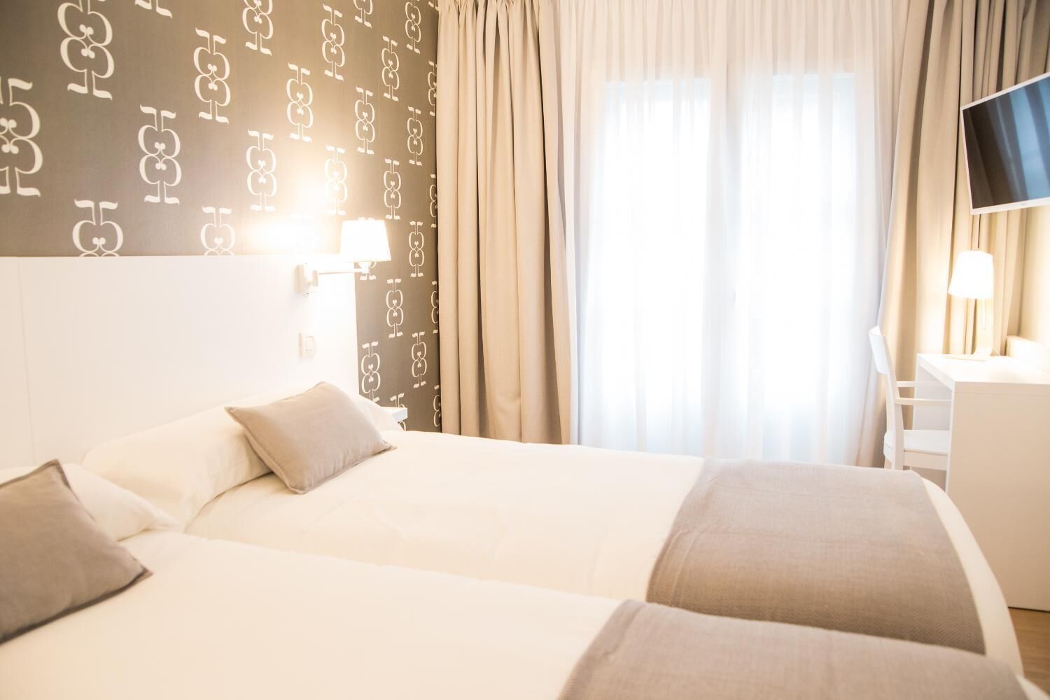 Habitación de hotel con dos camas, un escritorio y un televisor.