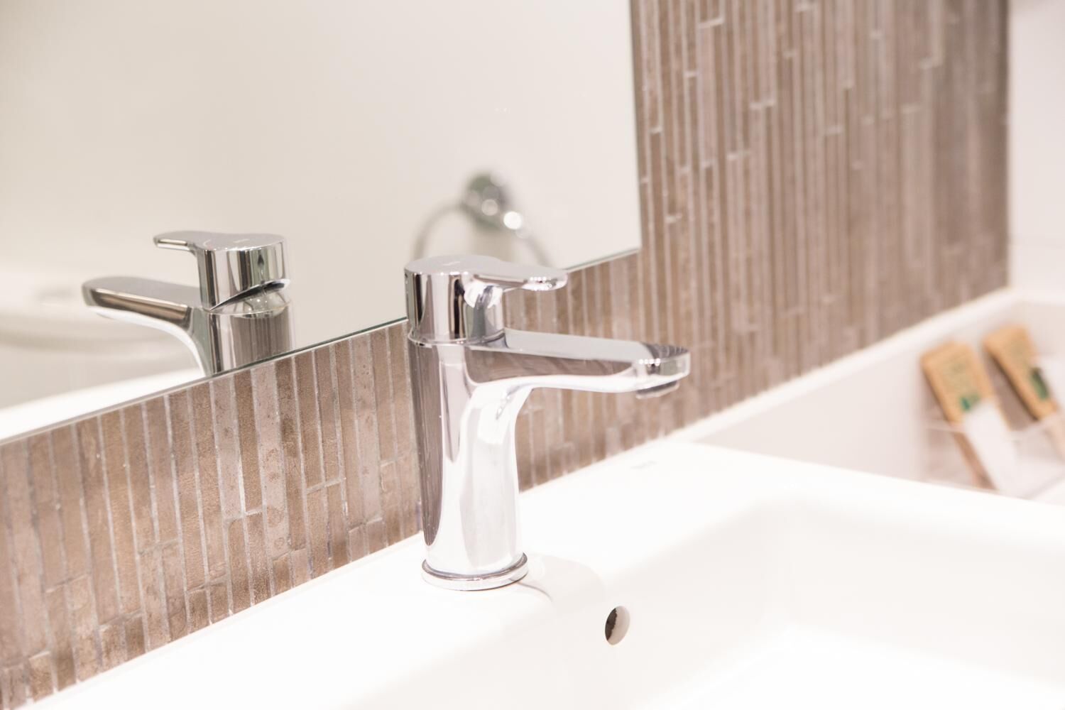 A bathroom with a modern chrome faucet and a mirror with a textured backsplash.