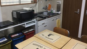 A small kitchenette with a microwave, sink, and storage bins. There is a window with blinds, a towel hanging on the wall, and a door to the right. - PoshtelOsaka240 (Osaka)
