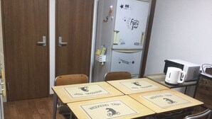A small kitchenette with a microwave, a coffee maker, and a refrigerator. There are four wooden tables with 'Weekend Trip' placards. - PoshtelOsaka240 (Osaka)
