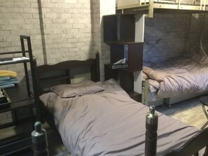 A dormitory room with bunk beds, a desk with a chair, and a small table.