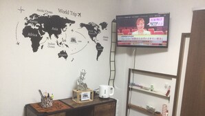 A room with a world map, a television, a wooden cabinet, and a shelf with various items. - PoshtelOsaka240 (Osaka)