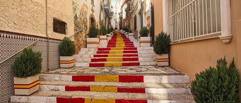 A narrow street with a staircase leading up to a building. The steps are painted in alternating red and yellow stripes.