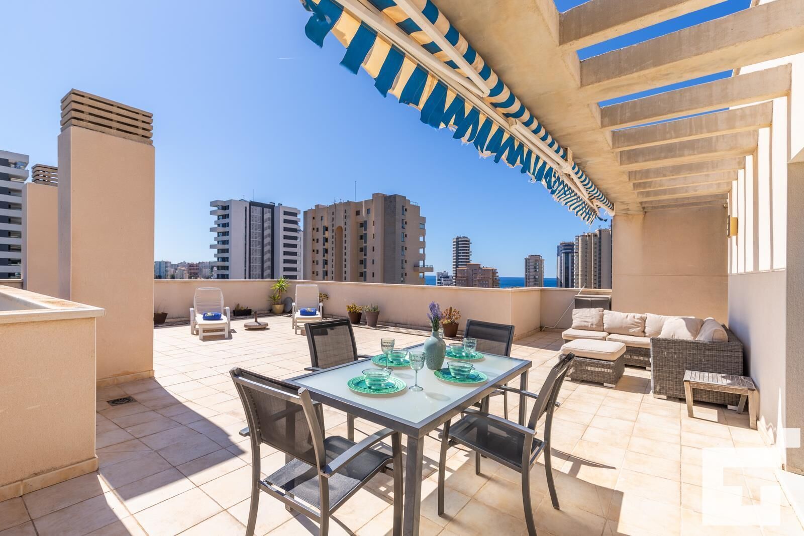 Terraço no telhado com área de refeições, cadeiras de descanso e vista para o horizonte da cidade.