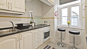 A modern kitchen with white cabinets, a stainless steel sink, a gas stove, and two bar stools.