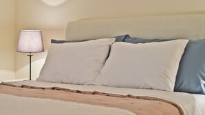 A neatly made bed with a beige headboard, white and blue pillows, and a brown throw blanket.