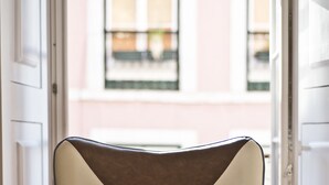 A chair with a geometric design, positioned in a doorway with open doors leading to a building with windows.