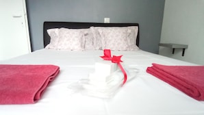 Una cama bien hecha con una colcha blanca, dos almohadas y dos toallas rojas dobladas a cada lado.
