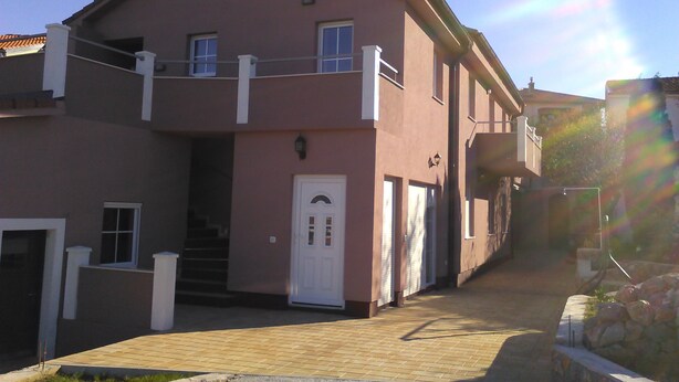 A two-story building with a pink facade, a white door, and a small balcony.