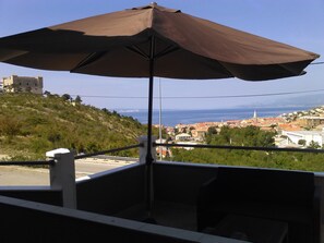 A balcony with a large umbrella, overlooking a coastal town with historic buildings and a hill with greenery. - Bmb Apartments - Senj (Senj)