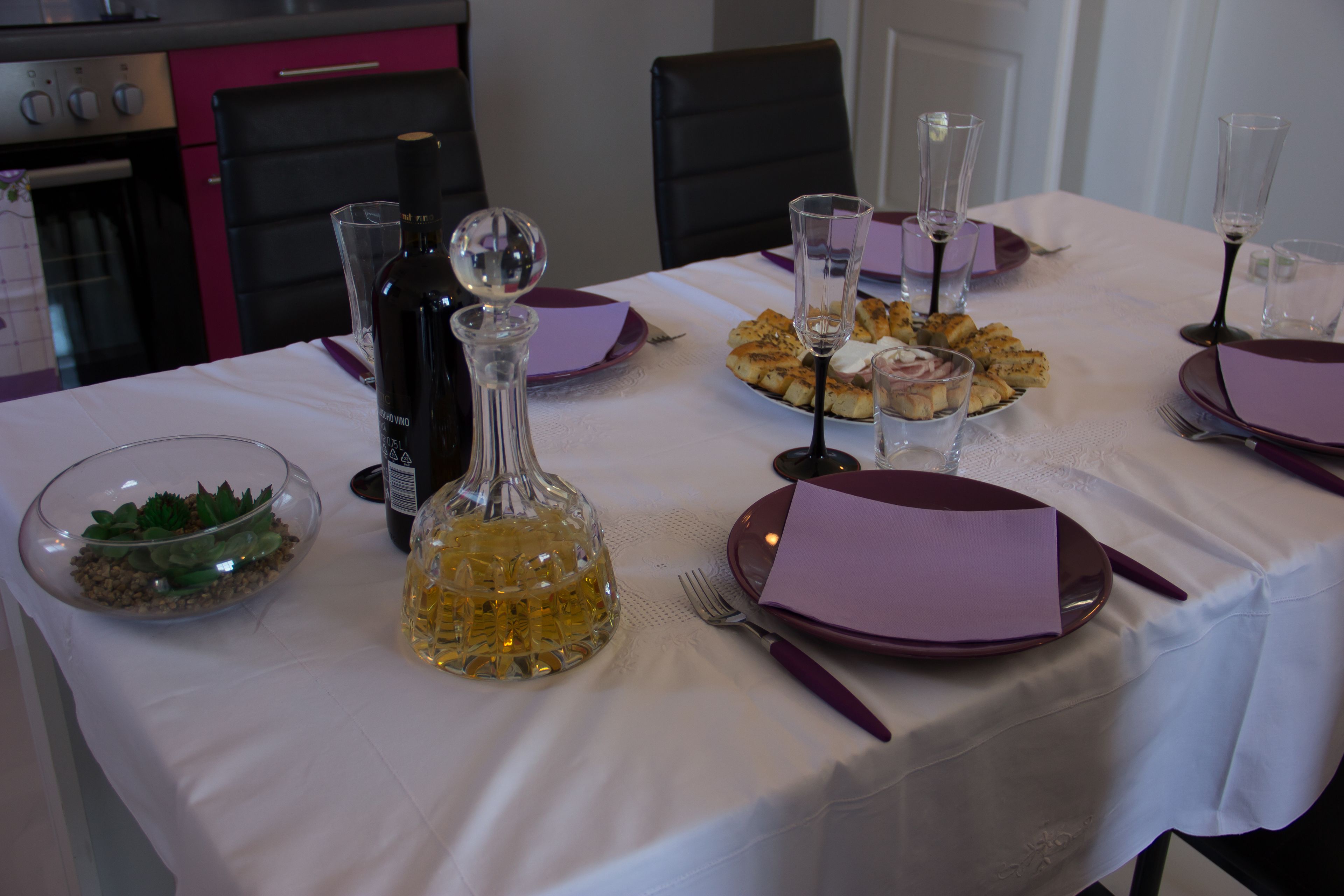 A dining table set with plates, glasses, and a bottle of wine.