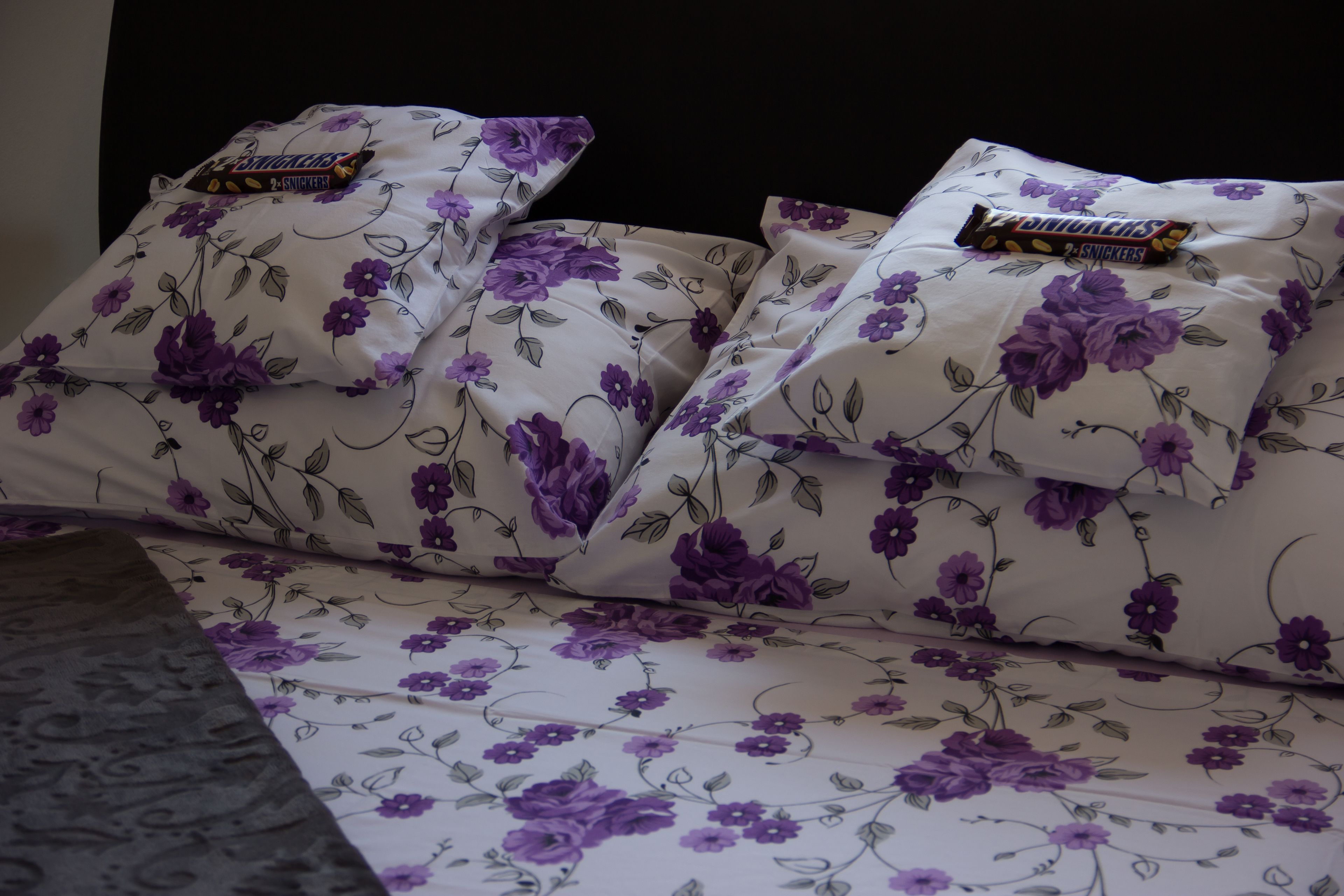 Ein Bett mit blumigem Bettzeug und zwei Snickersriegeln auf den Kopfkissen.
