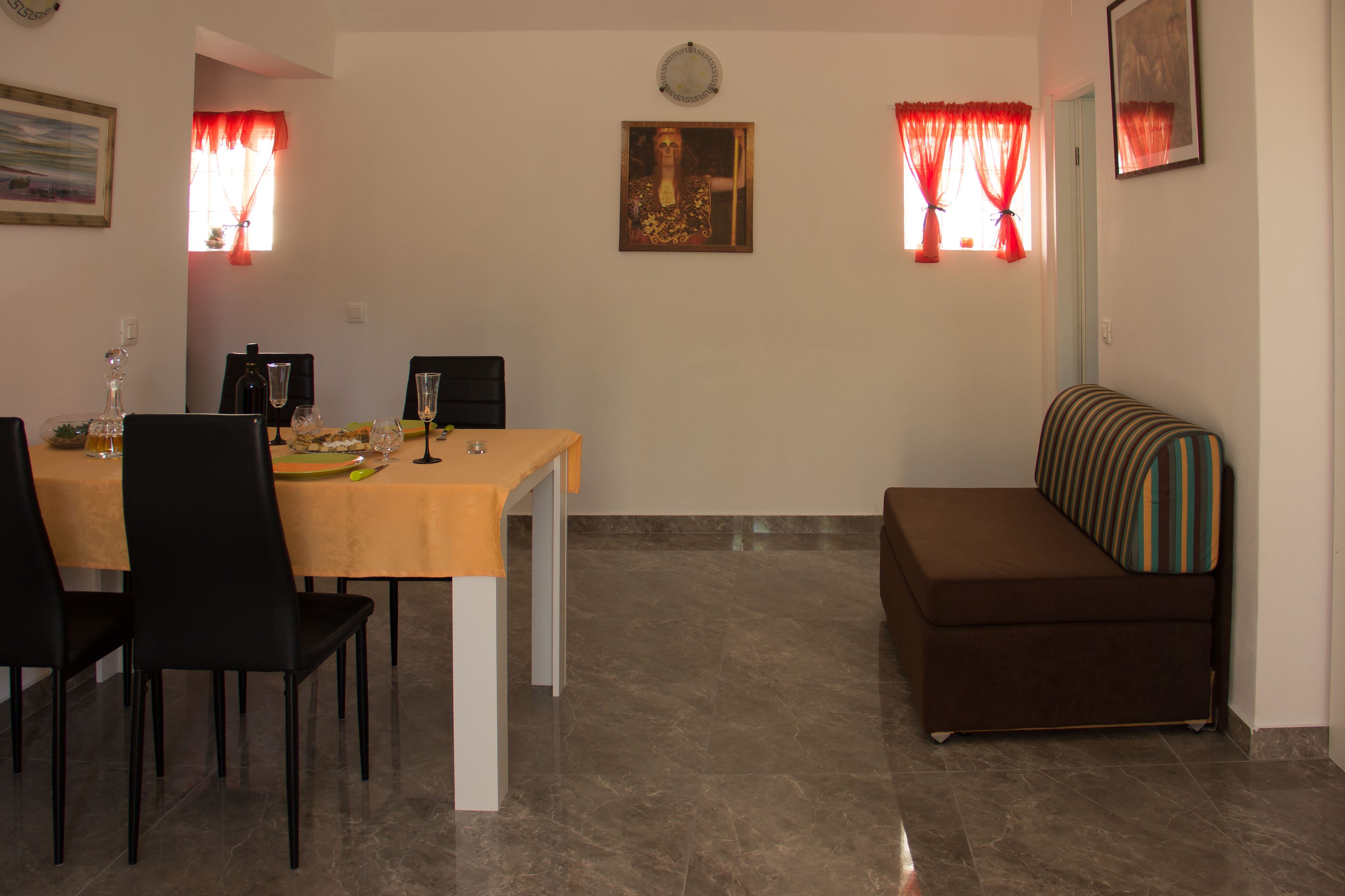 A dining area with a table set for four, a sofa, and a painting on the wall.