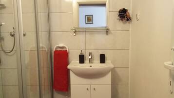 Um banheiro com box de vidro, pia branca com dois dosadores de sabonete pretos e uma toalha vermelha pendurada na parede.