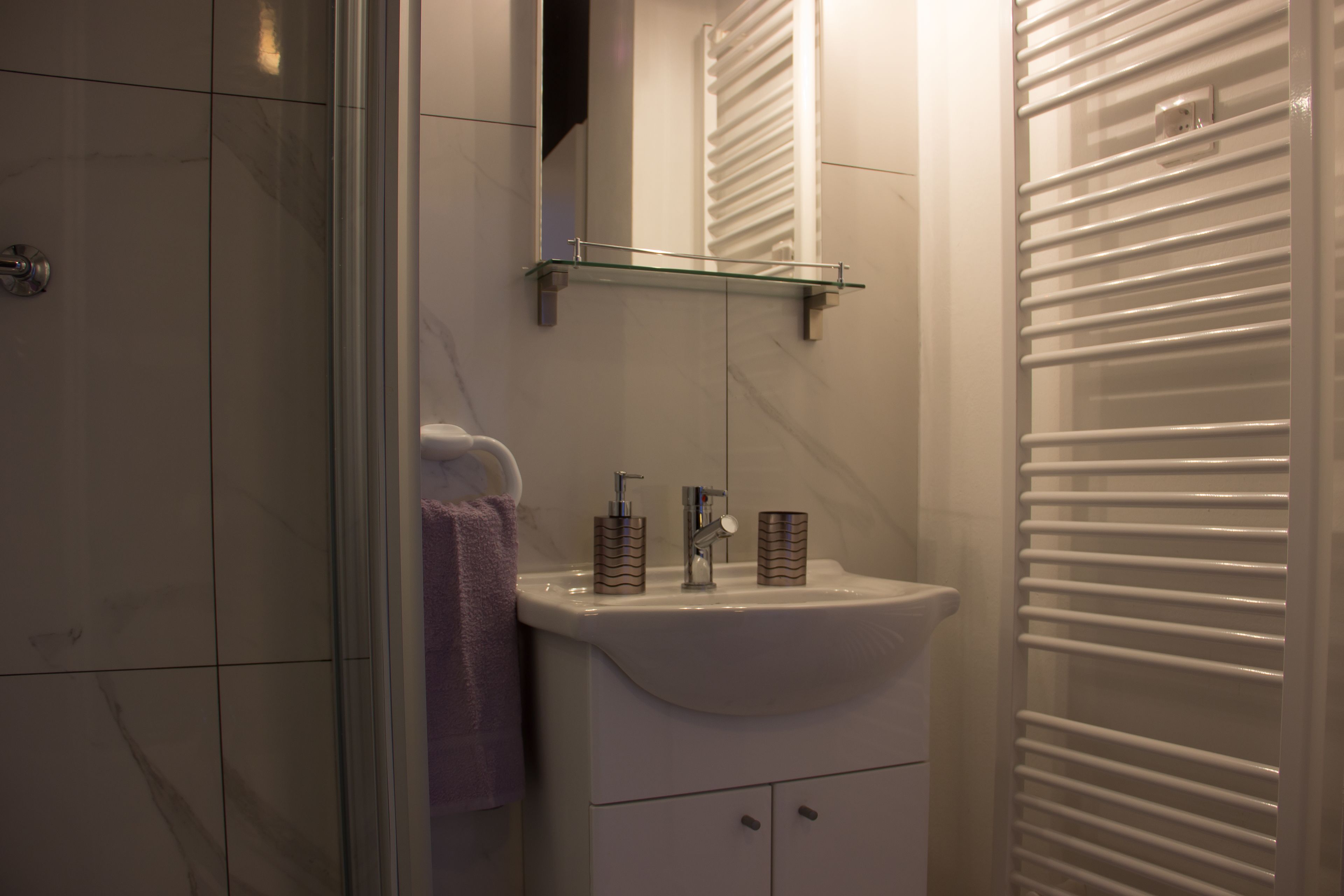 A bathroom with a glass shelf above the sink, a towel hanging on the wall, and a white tiled shower area.
