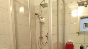 A bathroom with a glass-enclosed shower, a toilet with a red seat, and a sink with a red towel.