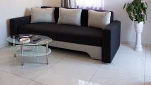 Una sala de estar moderna con un sofá negro, tres cojines, una mesa de centro de vidrio y una planta en maceta.